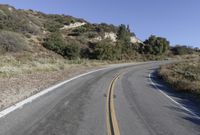 an empty country road on a hillside side surrounded by mountains and grasses is deserted yet it has just passed