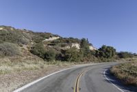 an empty country road on a hillside side surrounded by mountains and grasses is deserted yet it has just passed