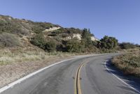 an empty country road on a hillside side surrounded by mountains and grasses is deserted yet it has just passed