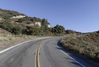 an empty country road on a hillside side surrounded by mountains and grasses is deserted yet it has just passed