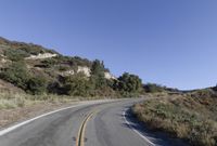 an empty country road on a hillside side surrounded by mountains and grasses is deserted yet it has just passed