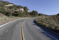 an empty country road on a hillside side surrounded by mountains and grasses is deserted yet it has just passed