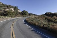 an empty country road on a hillside side surrounded by mountains and grasses is deserted yet it has just passed