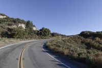 an empty country road on a hillside side surrounded by mountains and grasses is deserted yet it has just passed