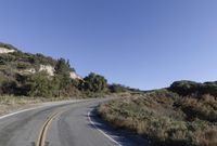 an empty country road on a hillside side surrounded by mountains and grasses is deserted yet it has just passed