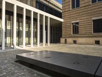 a empty courtyard with stone benches in front of it on a brick floor in front of the building