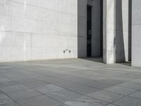 an empty courtyard with the doors open on a building side view of this building has a large wall with two vertical columns at one end and there is a hole in front