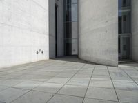 an empty courtyard with the doors open on a building side view of this building has a large wall with two vertical columns at one end and there is a hole in front