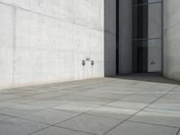 an empty courtyard with the doors open on a building side view of this building has a large wall with two vertical columns at one end and there is a hole in front