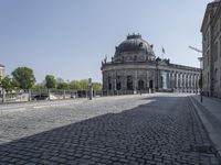 an empty courtyard outside a building with many buildings in the background, including a dome