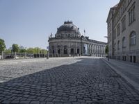 an empty courtyard outside a building with many buildings in the background, including a dome