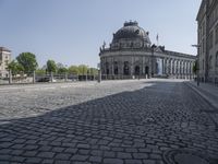 an empty courtyard outside a building with many buildings in the background, including a dome