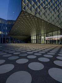 an empty courtyard in front of a large building in the evening light, with a black and white floor and circular pattern