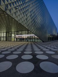 an empty courtyard in front of a large building in the evening light, with a black and white floor and circular pattern