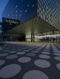 an empty courtyard in front of a large building in the evening light, with a black and white floor and circular pattern