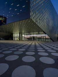 an empty courtyard in front of a large building in the evening light, with a black and white floor and circular pattern