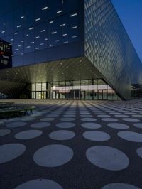 an empty courtyard in front of a large building in the evening light, with a black and white floor and circular pattern