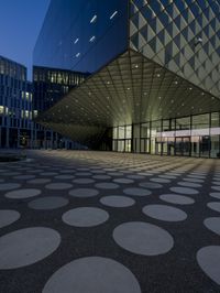 an empty courtyard in front of a large building in the evening light, with a black and white floor and circular pattern