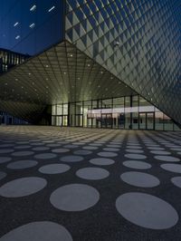 an empty courtyard in front of a large building in the evening light, with a black and white floor and circular pattern