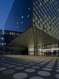 an empty courtyard in front of a large building in the evening light, with a black and white floor and circular pattern