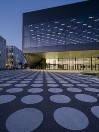 an empty courtyard in front of a large building in the evening light, with a black and white floor and circular pattern