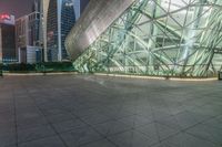 empty courtyard in front of building lit up at night in large city park area with cityscape behind