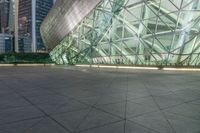 empty courtyard in front of building lit up at night in large city park area with cityscape behind