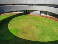 an empty courtyard with grass, a concrete building and two circular windows and a grassy lawn