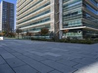 an empty courtyard in front of a very tall glass building with trees, plants and grass