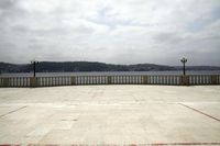 a large, empty patio overlooking the water and hills in the background is gray skies and a stone walkway with red markings