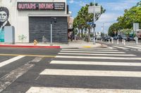 the white painted crosswalk on the street is empty and the sky is blue and the yellow line is painted with an image of an old man on the painting