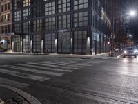 an empty crosswalk at night in a city with lights on and skyscrapers lit up