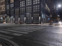 an empty crosswalk at night in a city with lights on and skyscrapers lit up