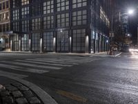 an empty crosswalk at night in a city with lights on and skyscrapers lit up