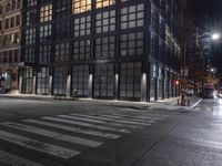 an empty crosswalk at night in a city with lights on and skyscrapers lit up