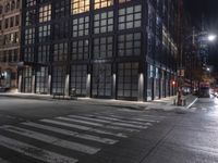 an empty crosswalk at night in a city with lights on and skyscrapers lit up