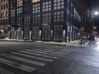 an empty crosswalk at night in a city with lights on and skyscrapers lit up