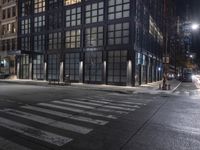 an empty crosswalk at night in a city with lights on and skyscrapers lit up