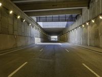 an empty dark street lined with concrete walls and lights above it in a tunnel with the road going under