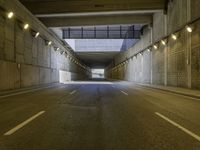 an empty dark street lined with concrete walls and lights above it in a tunnel with the road going under