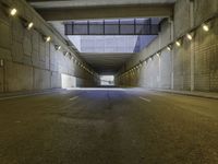 an empty dark street lined with concrete walls and lights above it in a tunnel with the road going under