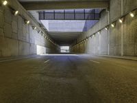 an empty dark street lined with concrete walls and lights above it in a tunnel with the road going under