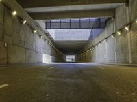 an empty dark street lined with concrete walls and lights above it in a tunnel with the road going under