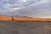 an empty empty desert with a telephone pole in the middle of it that has hills and a few clouds