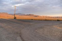 an empty empty desert with a telephone pole in the middle of it that has hills and a few clouds