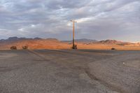 an empty empty desert with a telephone pole in the middle of it that has hills and a few clouds