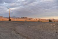 an empty empty desert with a telephone pole in the middle of it that has hills and a few clouds