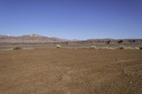 an empty dirt field with mountains in the distance in the desert under a blue sky