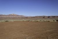 an empty dirt field with mountains in the distance in the desert under a blue sky