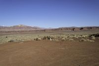 an empty dirt field with mountains in the distance in the desert under a blue sky